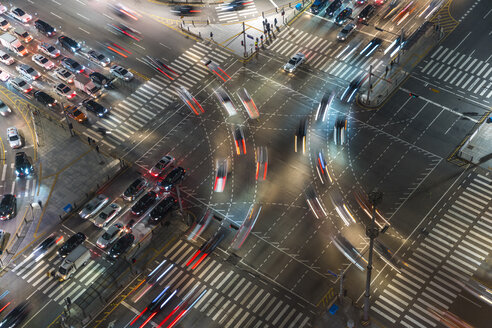 High angle view of busy urban street junction with pedestrian crossing at night, light trails of cars. - MINF08861