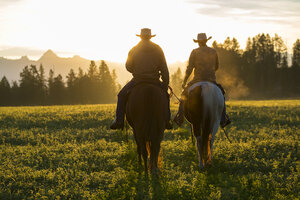 Zwei Cowboys auf Pferden in einer Prärie-Landschaft bei Sonnenuntergang. - MINF08882