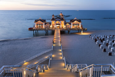 Wooden stairway and walkway leading across sandy beach towards illuminated building on a pier. - MINF08891