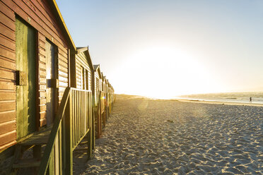 View along a row of colourful wooden beach huts on a long sandy beach at sunrise. - MINF08897