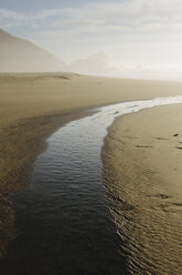 Small inlet on sandy beach near ocean at dusk, rocks and cliff in the distance. - MINF08901