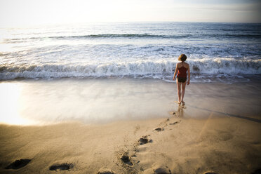 A young woman walks away from the camera into the surf on a quiet beach in Sayulita, Mexico. - AURF00575