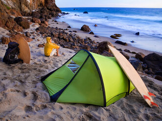 A young man camping on the beach waiting for surf. - AURF00669