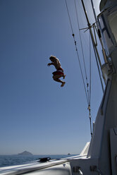 Ein junger Mann springt vom Dach eines Bootes in den Pazifischen Ozean mit einer Insel im Hintergrund. - AURF00715