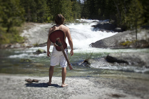 Ein junger Mann steht mit seiner Gitarre und blickt auf den Fluss und die Natur hinaus. - AURF00721