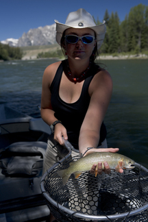 A young woman in a cowboy hat holding a fish net shows a cutthroat trout.  stock