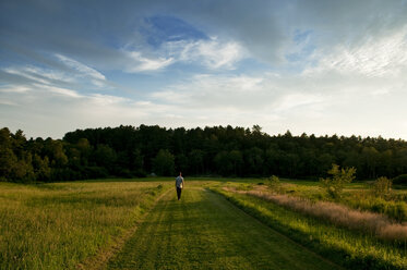 Ein junger Mann schlendert im Abendlicht einen grasbewachsenen Weg außerhalb des Acadia National Park in Maine entlang. - AURF00741