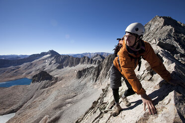 Ein junger Mann überquert eine ausgesetzte Gratlinie mit dem Gipfel im Rücken. - AURF00744