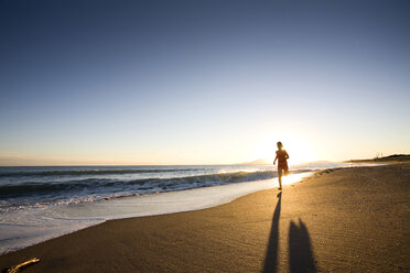 Eine junge Frau läuft bei Sonnenuntergang am Strand von Chiarone in der Toskana, Italien (Gegenlicht) - AURF00769