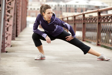 An athletic female in a purple jacket stretching along a bridge in Portland, Oregon. - AURF00797