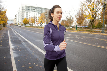 Eine sportliche Frau in einer lila Jacke läuft eine verlassene Straße in Portland, Oregon, entlang. - AURF00798