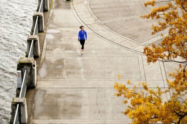 Eine sportliche Frau in einer blauen Jacke joggt an der Uferpromenade von Portland, Oregon. - AURF00799