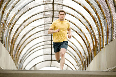 Ein sportlicher Mann joggt durch eine Fußgängerüberführung. - AURF00806