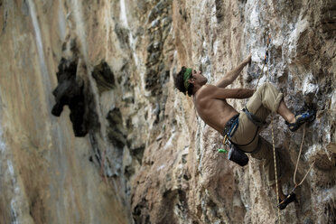 Adult male caucasian listening to MP3 player while climbing limestone cliffs in Thailand. - AURF00815