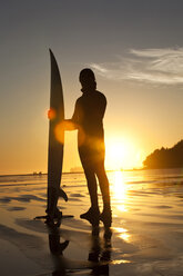 Mann steht mit Surfbrett bei Sonnenuntergang in British Columbia. - AURF00862