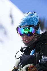 Ein Porträt eines Snowboarders, der lächelt, während sich in seiner Brille ein Schneemobil spiegelt, im Hinterland von Colorado. - AURF00883