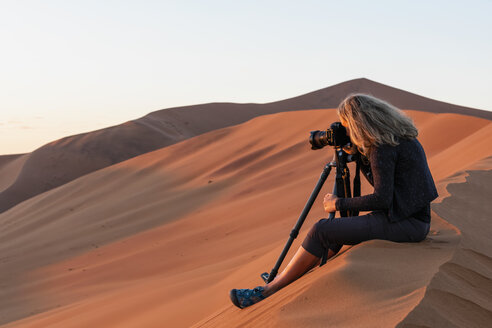 Africa, Namibia, Namib desert, Naukluft National Park, female photograper photographing at early morning light, sitting on sand dune - FOF10066