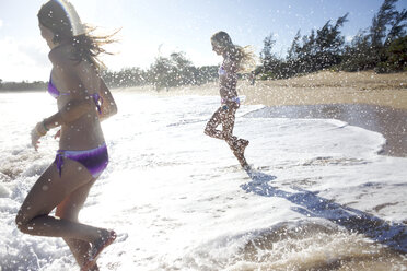 Zwei Mädchen im Vorschulalter rennen zum Wasser am Paia Beach, Maui, Hawaii, und lächeln, während sie nass werden. - AURF00946