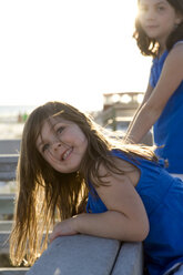 Zwei kleine Mädchen stehen auf einem Geländer an der Uferpromenade und blicken in die Kamera, die Sonne scheint auf ihre Haare. - AURF00956