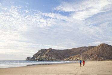 Two people walk down an empty beach under a blue sky. - AURF00972