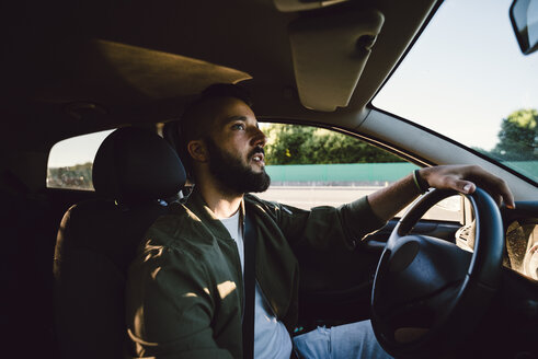 Bearded young man looking at rear-view mirror while driving car - RAEF02113