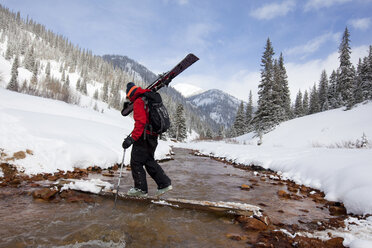Ein Mann trägt seine Skier über einen verschneiten Bergbach. - AURF00992