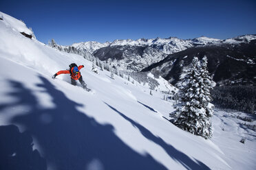 Ein sportlicher Snowboarder zieht an einem sonnigen Tag in Colorado frische Powder-Kurven im Backcountry. - AURF01019