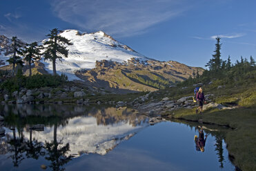 Ein Rucksacktourist wandert an einem alpinen Teich und dem Spiegelbild des Mt. Baker in der Wildnis des Mt. Baker im Bundesstaat Washington vorbei. - AURF01023
