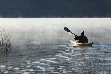 Ein sportlicher Mann im Ruhestand fährt bei Sonnenaufgang mit dem Kajak über einen nebligen See in Idaho. - AURF01040