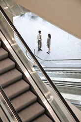 Ein gemischtrassiges Paar von Geschäftsleuten auf dem Weg zu einem Treffen in der Nähe einer Rolltreppe. - MINF08936