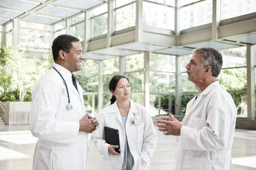 Mixed race group of doctors meeting in lobby of large hospital - MINF08950