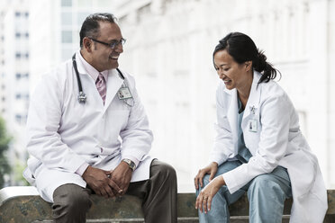 Ein hispanischer Mann und eine asiatische Frau beraten sich in einem Krankenhaus über einen Fall. - MINF08955