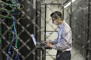 Hispanic man technician doing diagnostic tests on computer servers in a large server farm. - MINF08966