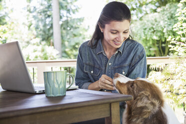 Mixed race Caucasian woman working on her lap top at home with her dog. - MINF08973