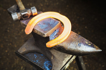 Ein rot glühendes, erhitztes Metallhufeisen und ein Hammer auf einem Amboss, die Ausrüstung eines Schmieds. - MINF09020