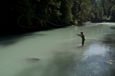 A man casts in a river wearing waders while fly fishing in Squamish, British Columbia. - AURF01139