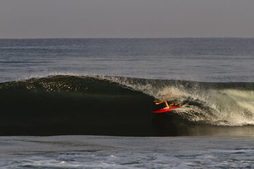 Ein männlicher Surfer auf einem roten Brett fährt beim Surfen in Pascuales, Mexiko, durch ein kleines sauberes Fass. - AURF01151