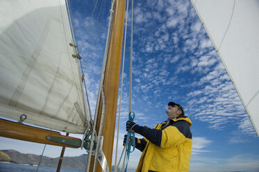 A man adjusts the rigging on his yacht. - AURF01152