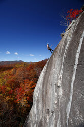 Ein Mann, der sich abstützt, steigt eine Granitwand hinab, die von Herbstfarben umgeben ist. - AURF01156