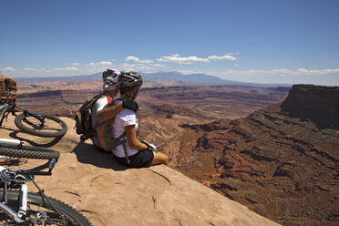 A mountain biking couple takes a break to enjoy the view from the edge of a cliff. - AURF01185