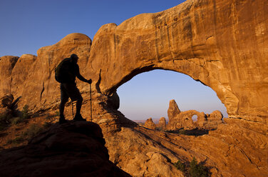 Ein Wanderer mit Silhouette steht vor einem Bogen im Arches National Park, Utah. - AURF01201