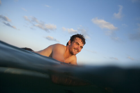 Ein lächelnder männlicher Surfer auf seinem Brett im Wasser bei Sonnenuntergang in Baja, Mexiko. - AURF01202