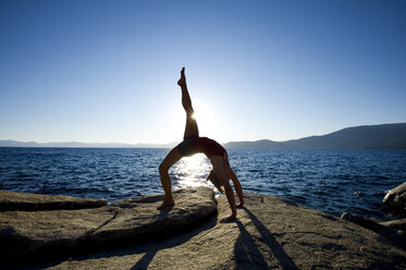 Die Silhouette einer jungen Frau, die auf einem Granitfelsen am Ostufer des Lake Tahoe, NV, Yoga macht. - AURF01214