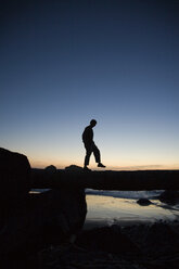 Die Silhouette eines Mannes, der nach Sonnenuntergang an einem Baumstamm an der Küste von Kalifornien entlangläuft. - AURF01216