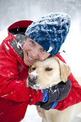 Eine Frau umarmt ihren Hund liebevoll an einem verschneiten Wintertag. - AURF01235