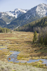 A young man paddles his small, inflatable raft through a high alpine meadow near the headwaters of the Salmon River in Idaho. - AURF01240
