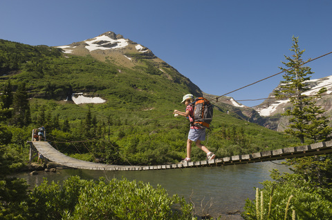 Ein junges Mädchen wandert über eine Hängebrücke im Glacier National Park, Montana., lizenzfreies Stockfoto