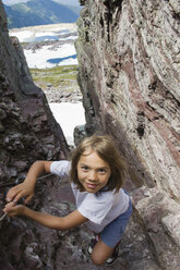 A young girl makes her way up a narrow slot in a cliff while hiking in Glacier National Park, Montana. - AURF01243