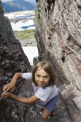 Ein junges Mädchen bahnt sich beim Wandern im Glacier National Park, Montana, einen Weg durch einen engen Schlitz in einer Klippe. - AURF01243