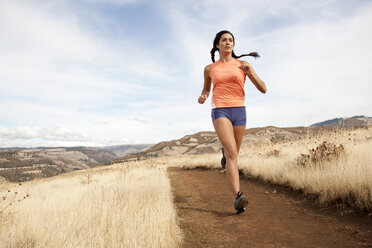 An athletic female jogs on a dirt trail on an autumn day. - AURF01263
